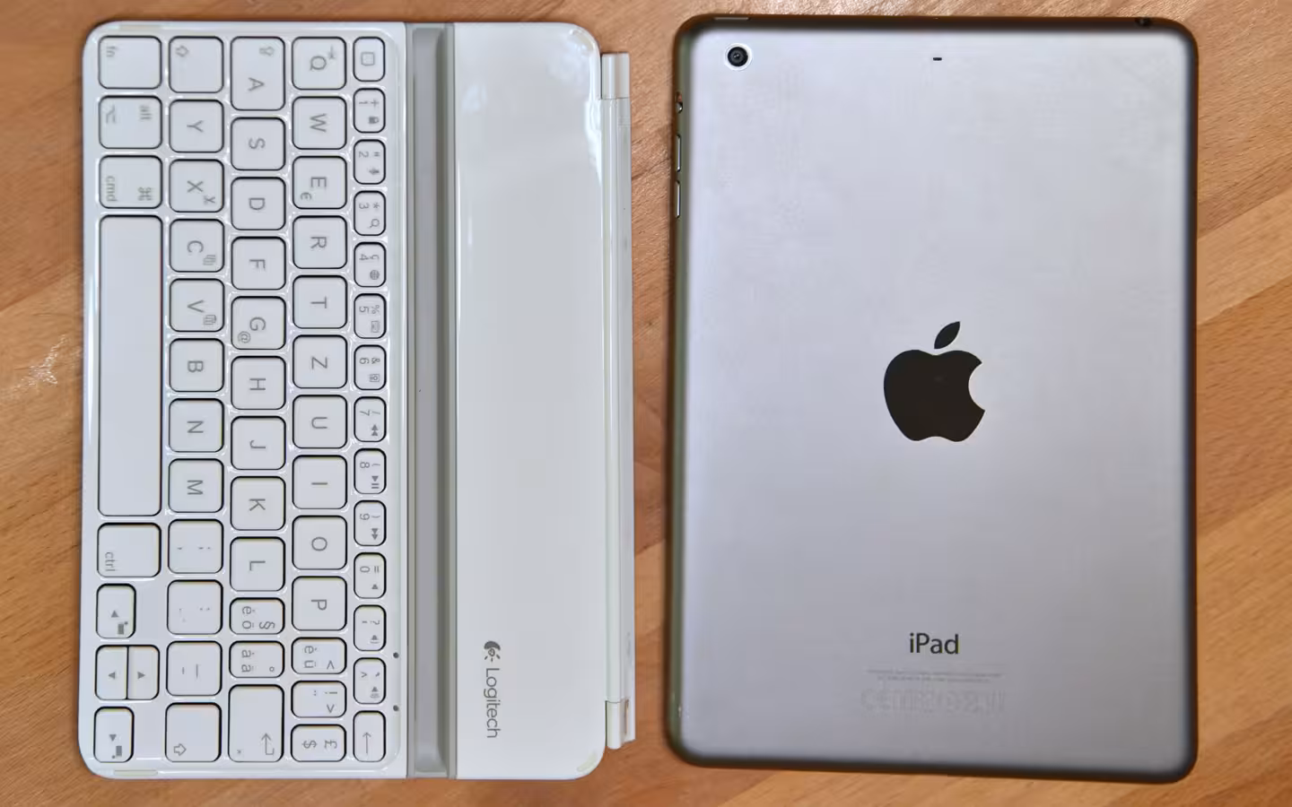 An Apple iPad mini beside a white Logitech keyboard on a wooden surface