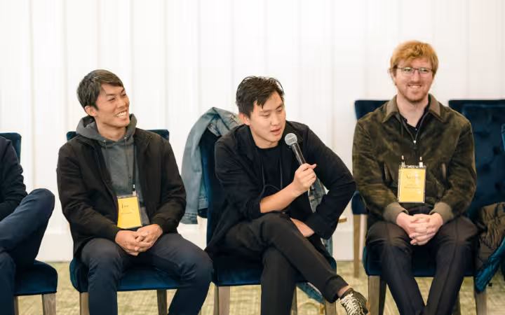 Three men, including Alexandr Wang, sit on a panel as one speaks into a microphone.