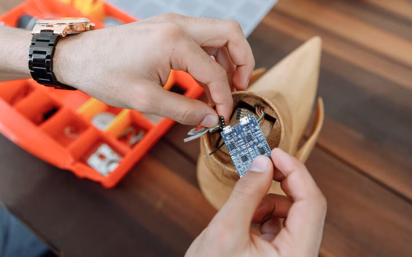 Hands adjust a microcontroller board inside a small DIY electronics project.
