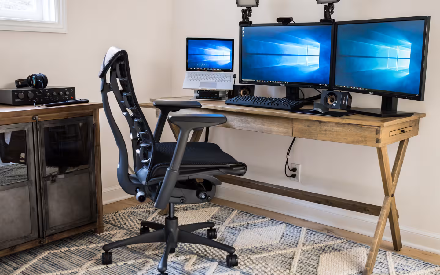 A Microsoft Surface Book 2 beside two monitors showing Windows 10 desktops