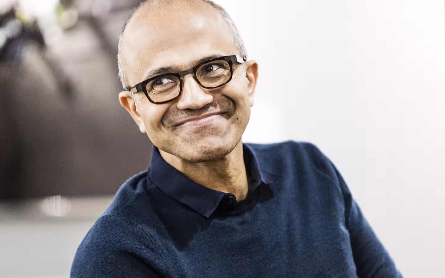 Microsoft CEO Satya Nadella smiling in glasses and a navy sweater