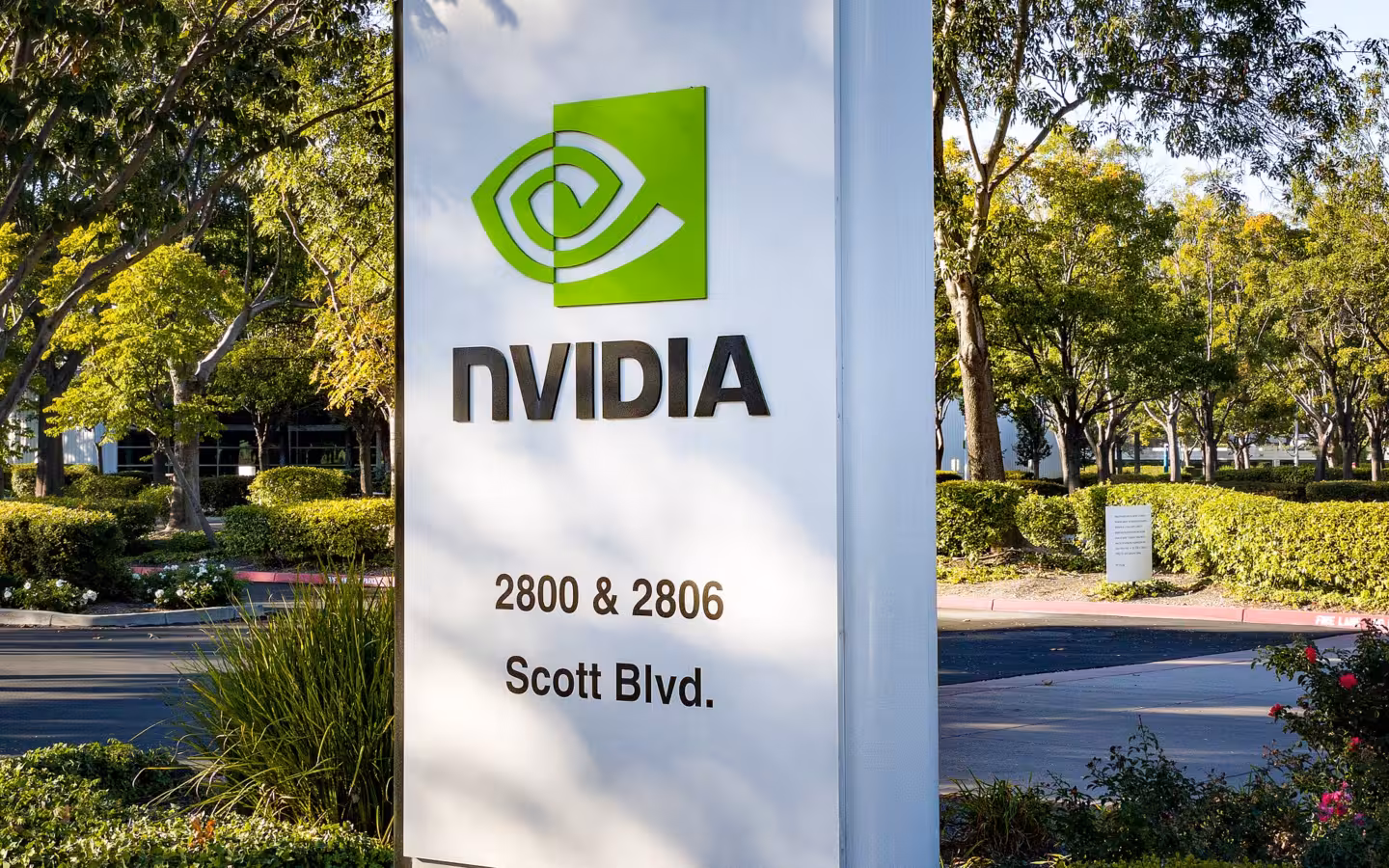 Nvidia headquarters sign beside a landscaped road and trees in Santa Clara.