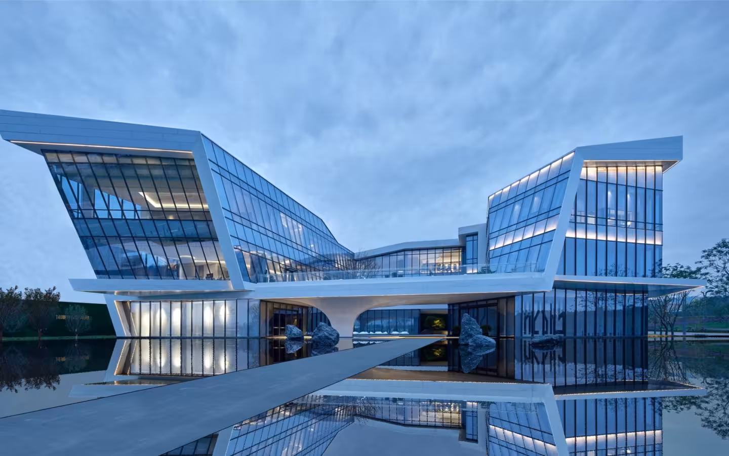 A modern glass building reflected in a still pool of water.