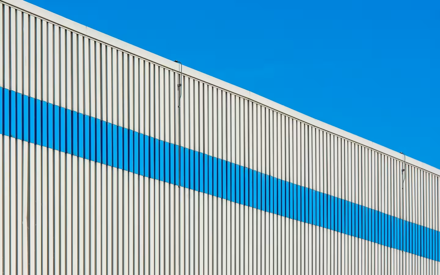 A sunlit industrial building facade with a bold blue stripe.