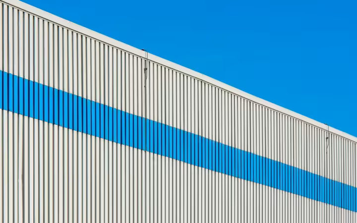 A sunlit industrial building facade with a bold blue stripe.
