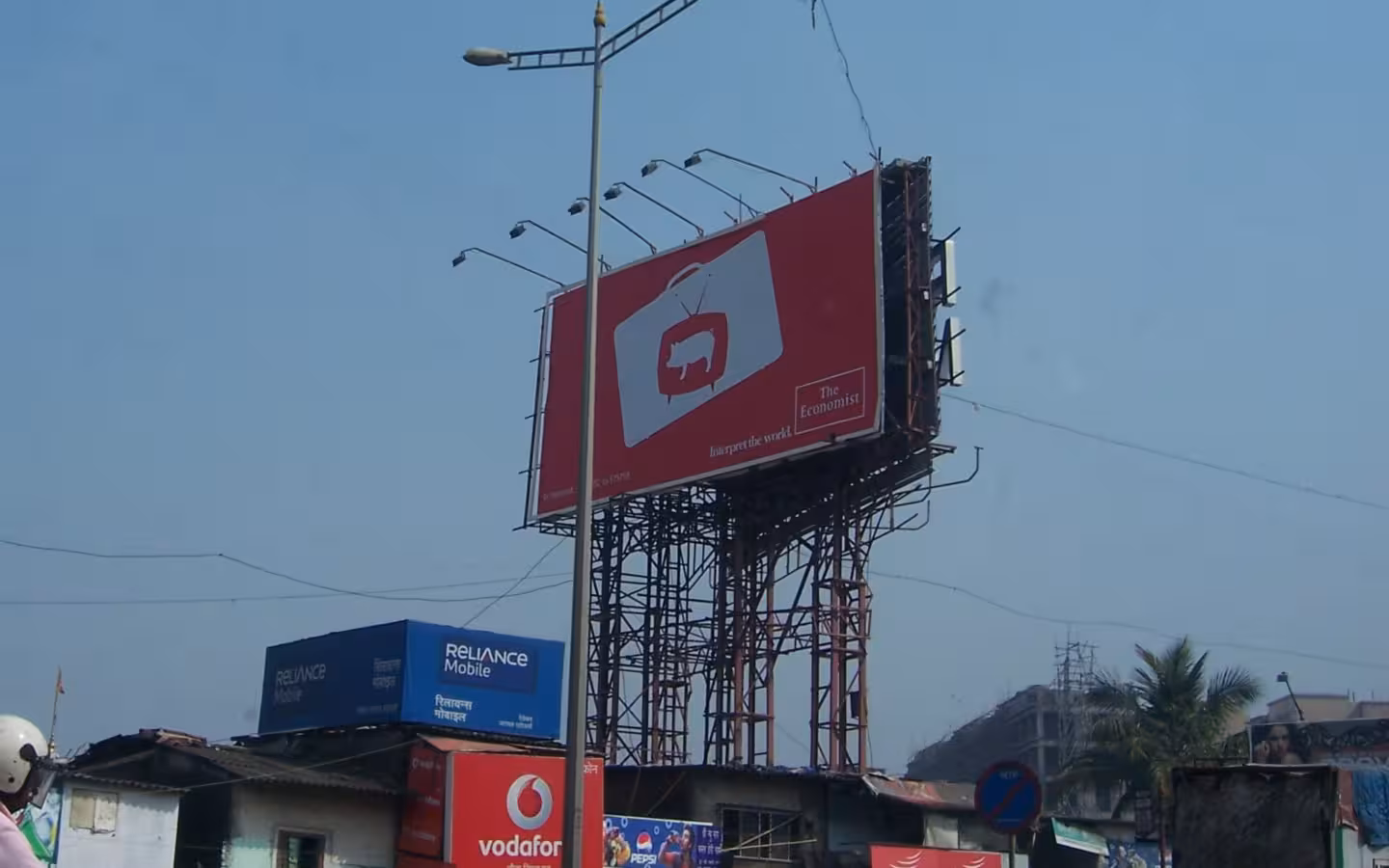 A red Economist billboard rises above a cluttered street in India.