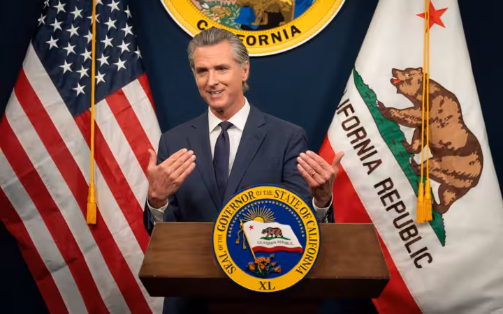 Governor Gavin Newsom speaks at a lectern between American and California flags.