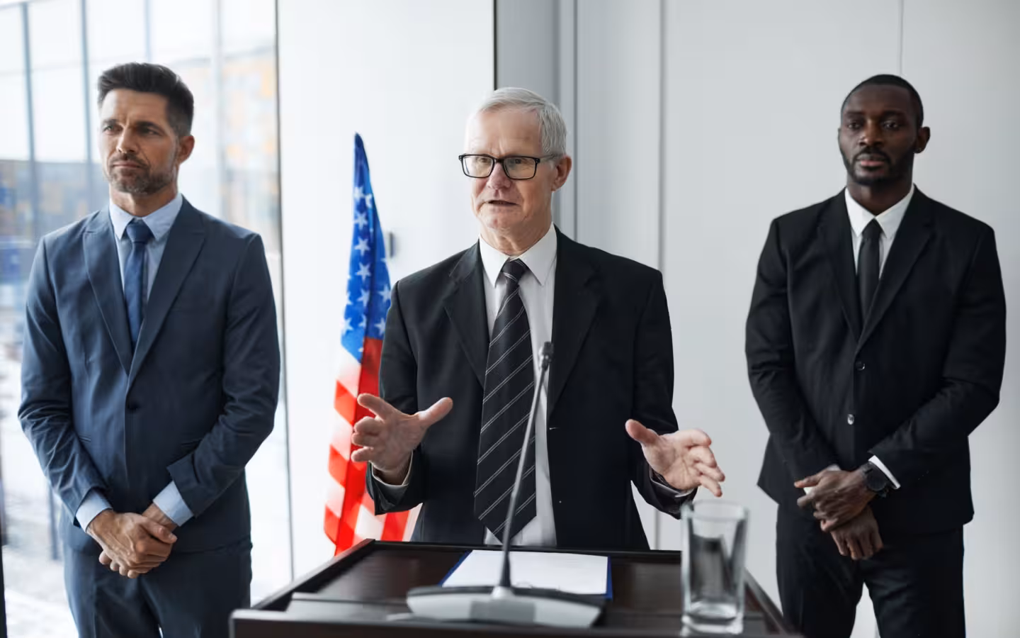 Three business professionals stand by a lectern and an American flag.