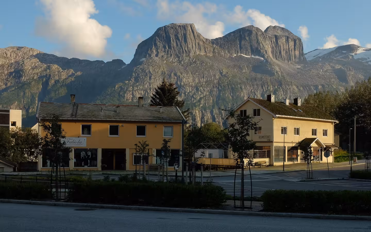 Buildings and a street in Glomfjord beneath steep, sunlit mountains