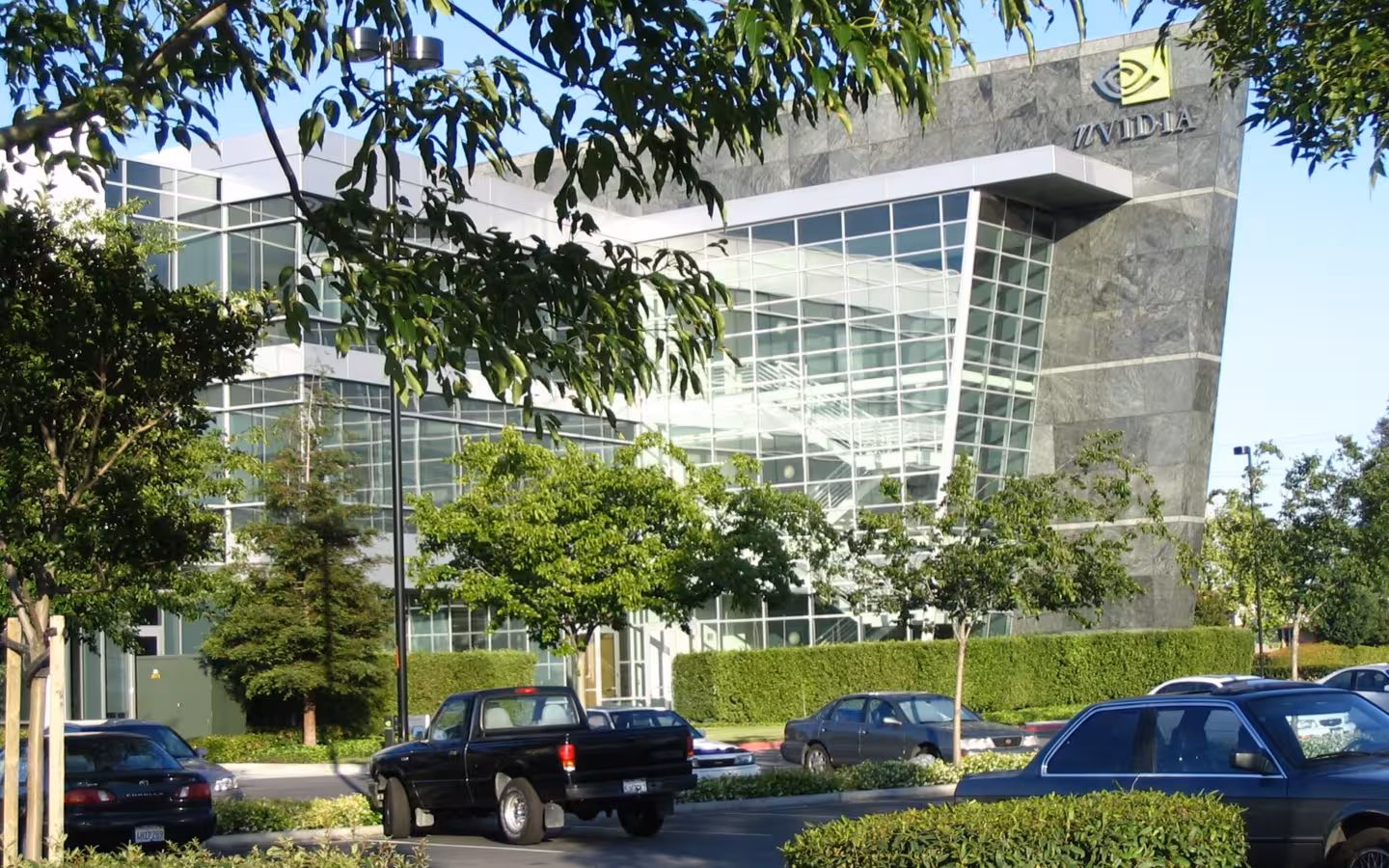 NVIDIA headquarters behind trees and parked cars, with a glass-fronted entrance
