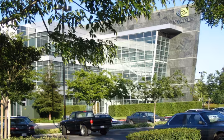 NVIDIA headquarters behind trees and parked cars, with a glass-fronted entrance