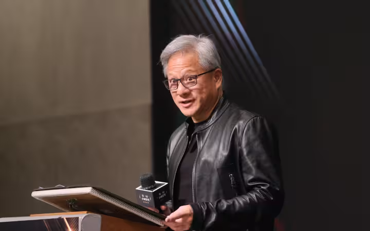 Jensen Huang speaks into a microphone beside a lectern.