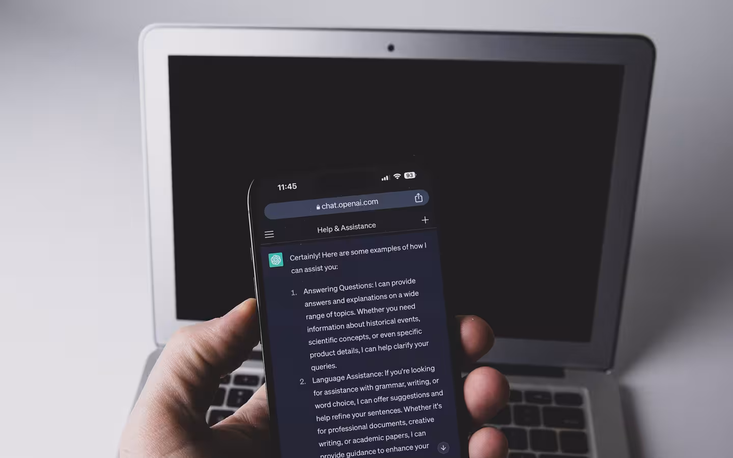 Smartphone displaying the ChatGPT app held in front of a laptop