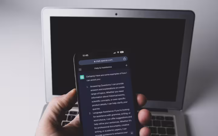 Smartphone displaying the ChatGPT app held in front of a laptop