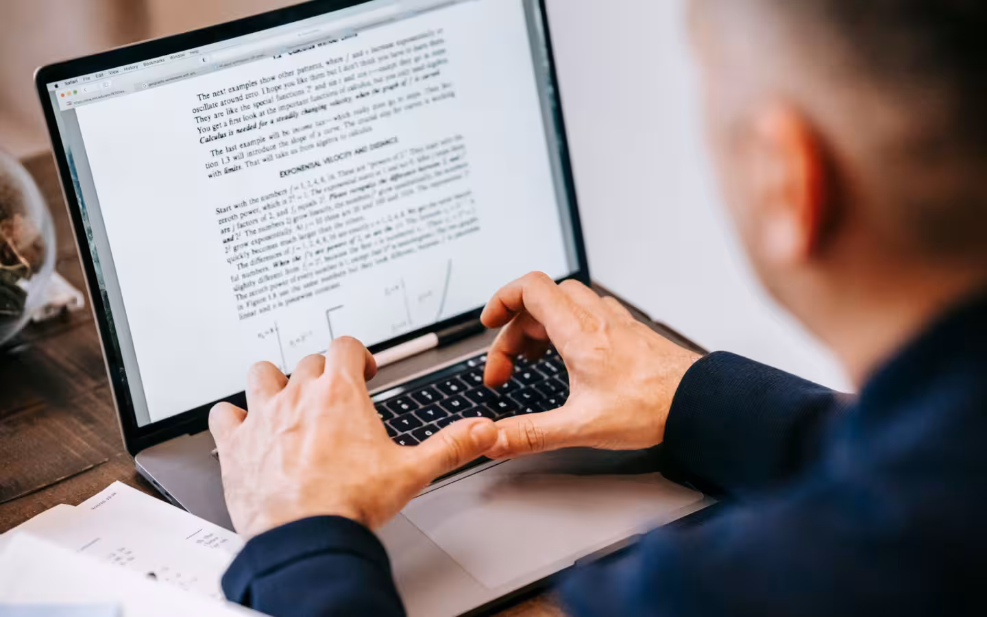 A man typing on a laptop displaying text in a home office.