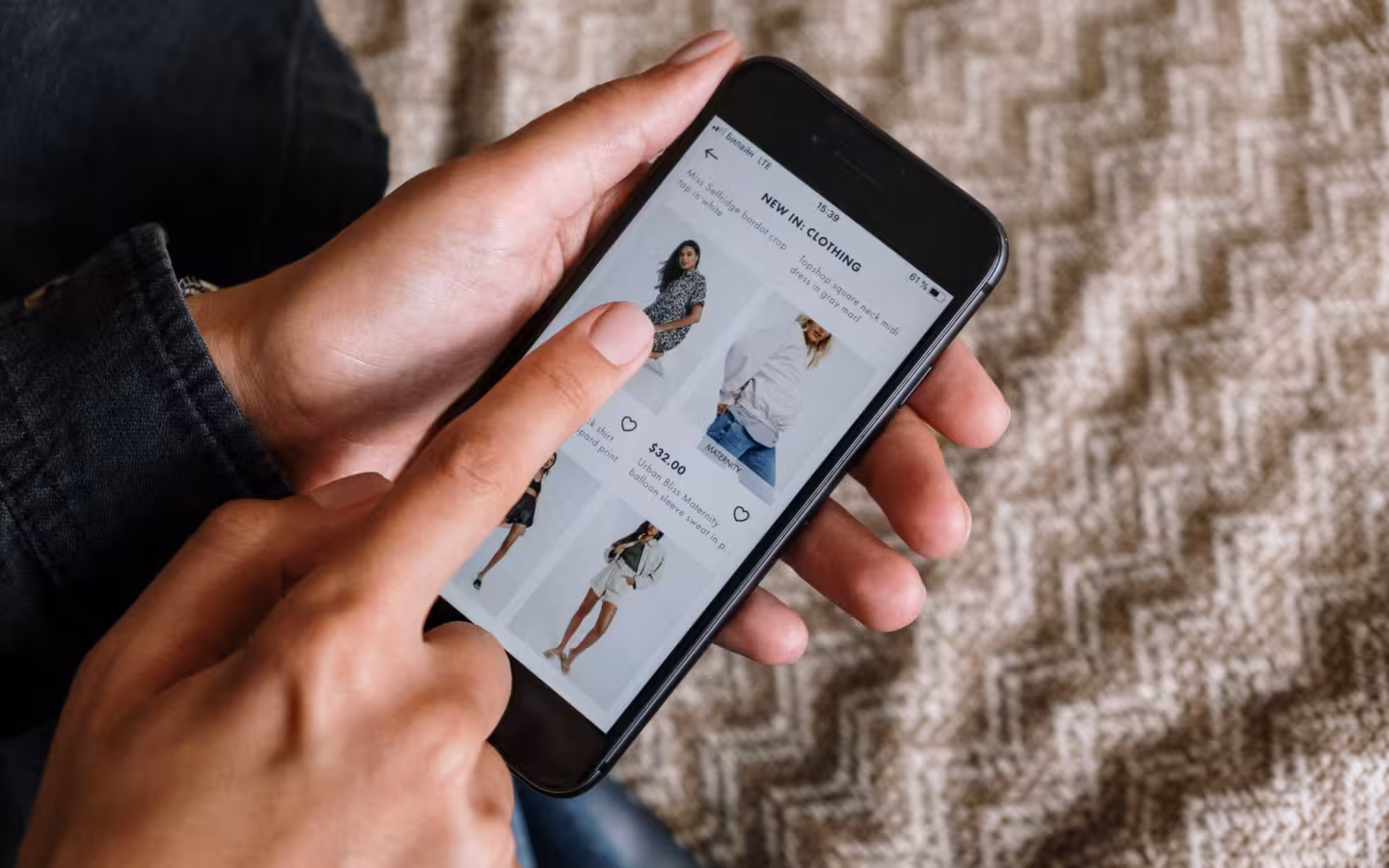 Hands browsing clothing listings on a smartphone over a patterned rug