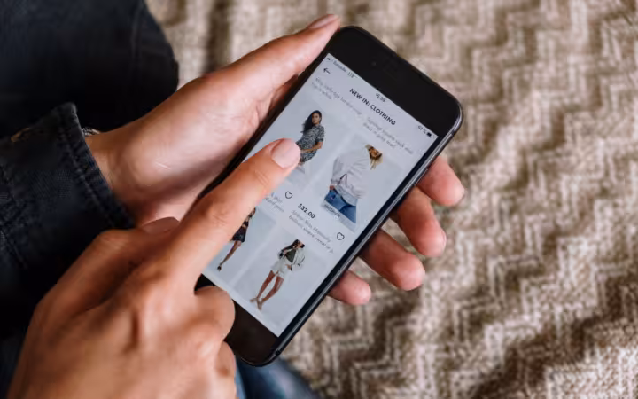 Hands browsing clothing listings on a smartphone over a patterned rug