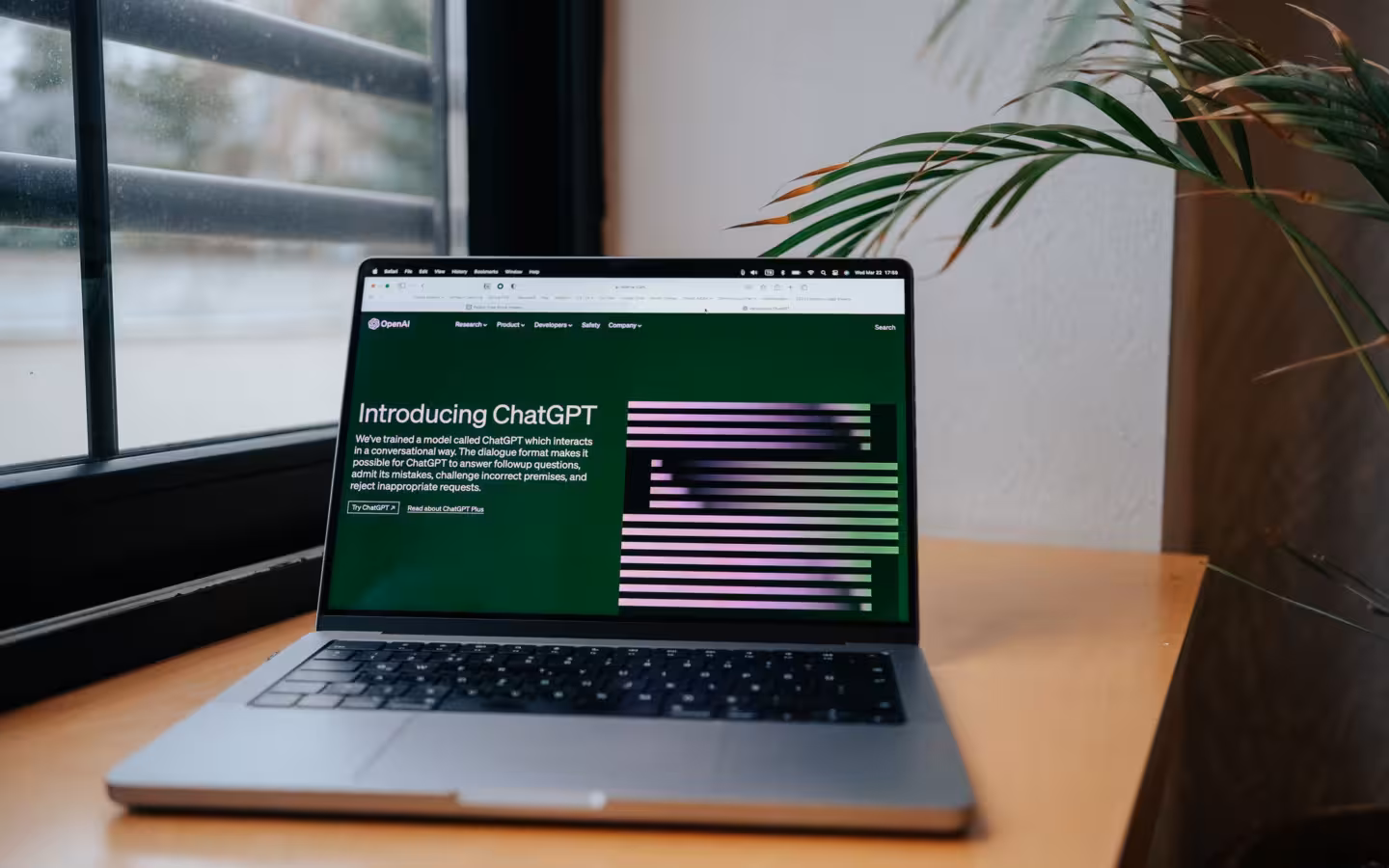 A laptop displaying OpenAI’s ChatGPT page on a desk beside a window.