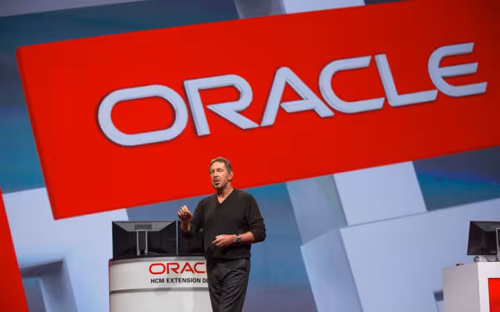 Larry Ellison speaking onstage beneath a large Oracle sign