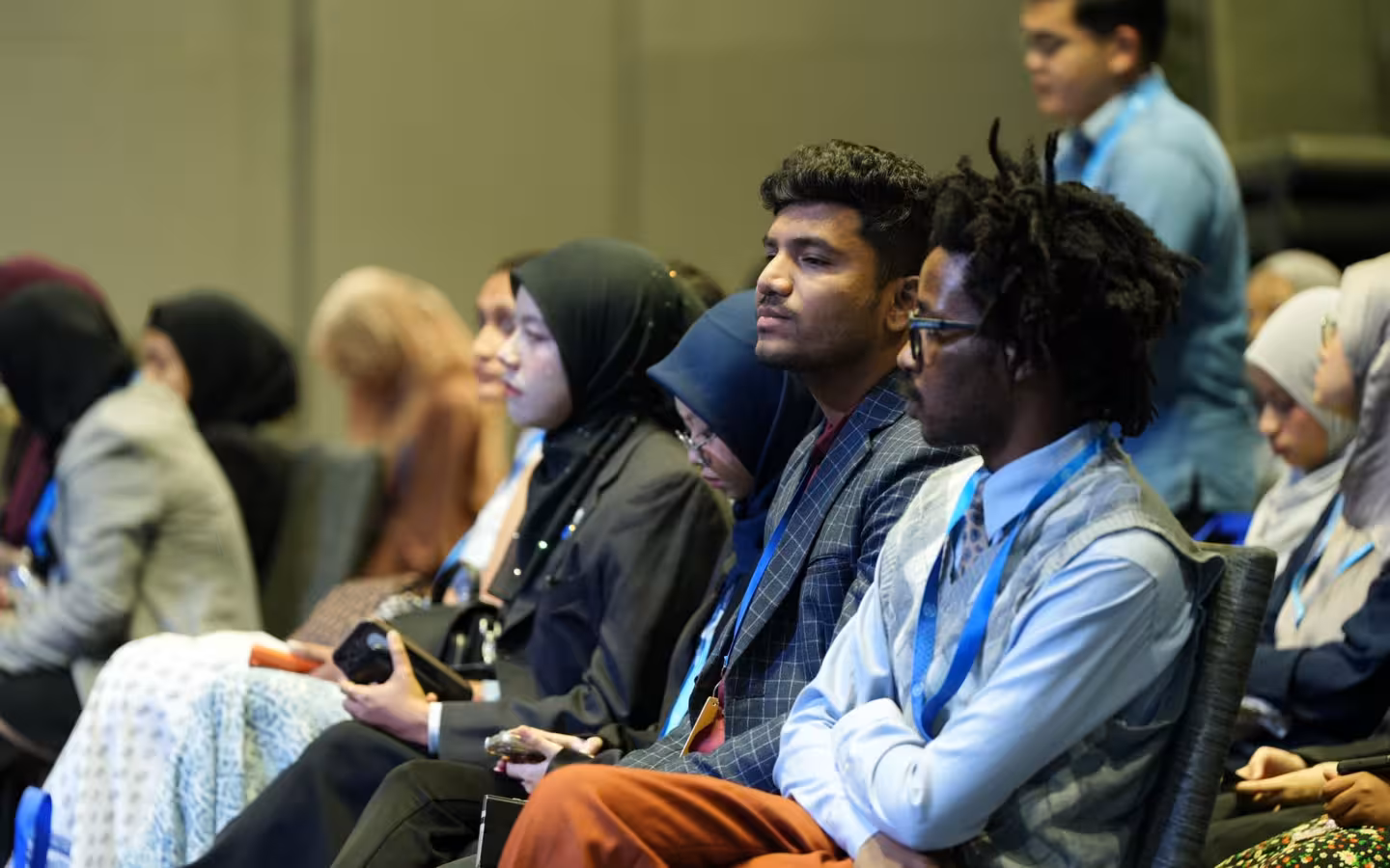 Conference attendees seated in rows, listening in an indoor hall.