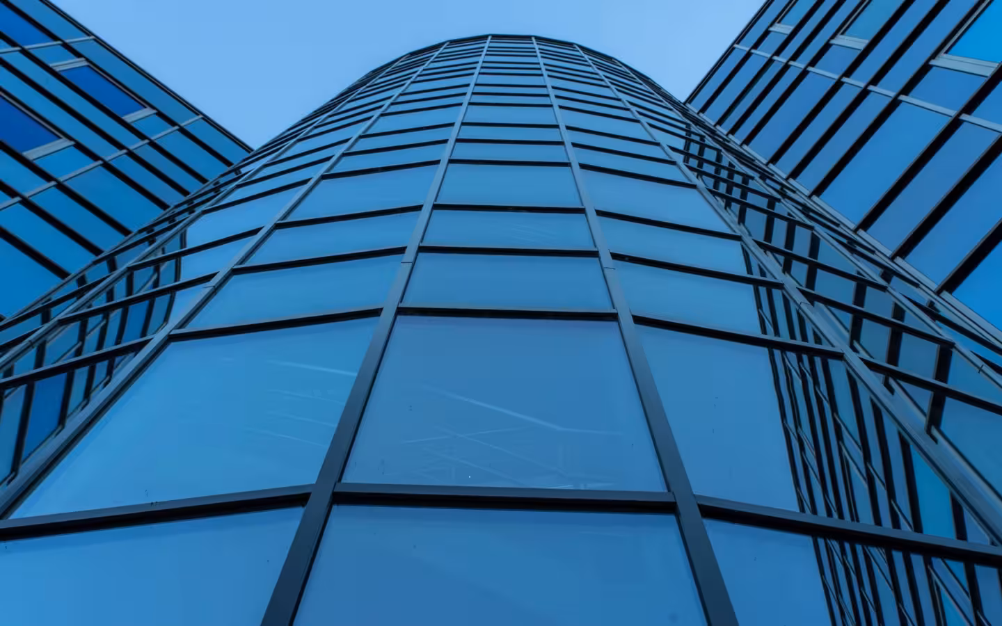 An upward view of a contemporary skyscraper’s blue reflective glass facade.
