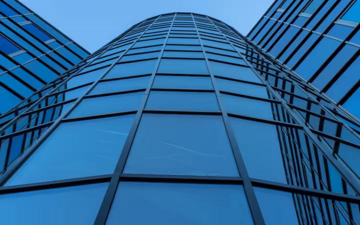 An upward view of a contemporary skyscraper’s blue reflective glass facade.