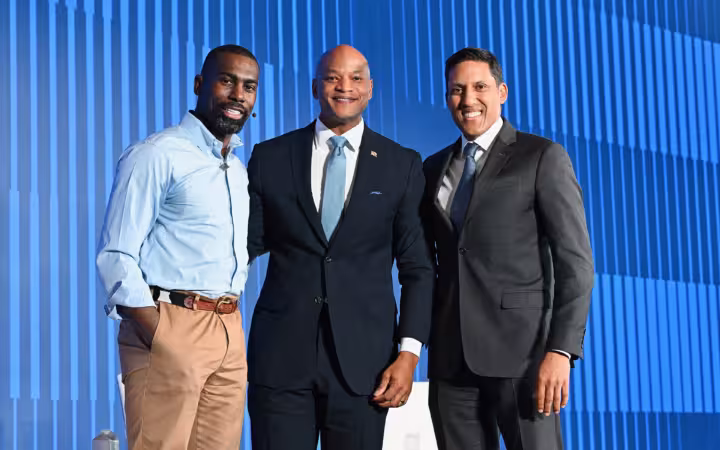 Rajiv Shah and two other men pose before a blue stage backdrop.