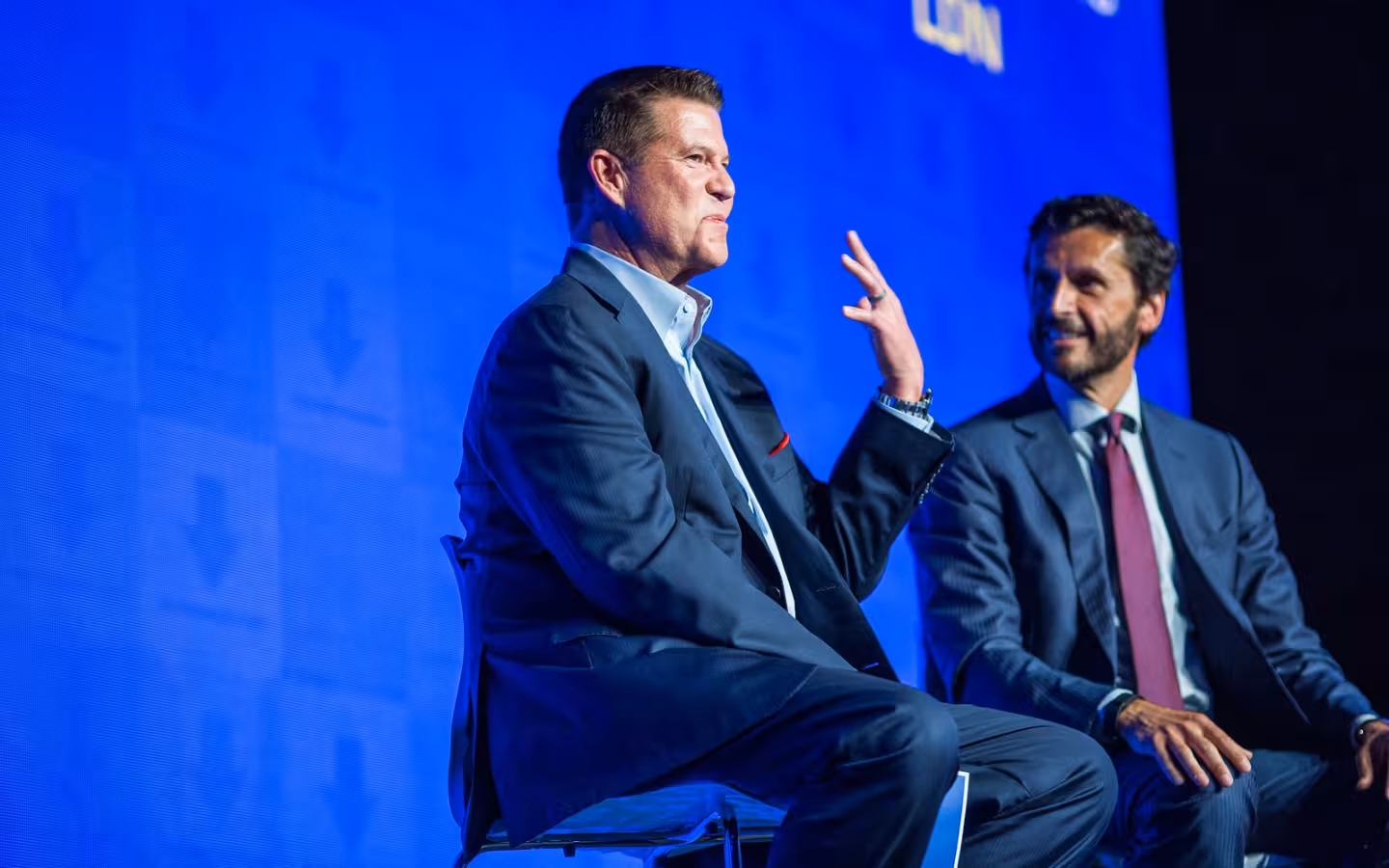 Keith Krach and Miguel Milano seated onstage against a blue backdrop