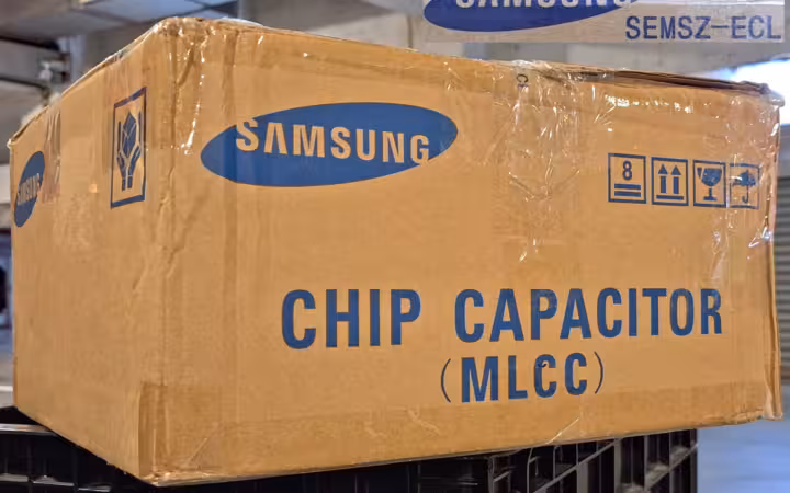 A Samsung Electro-Mechanics chip capacitor carton rests on black crates.