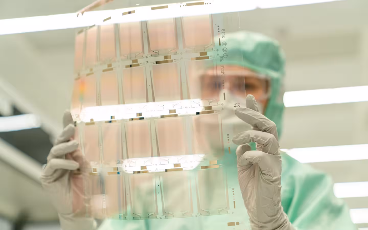 Scientist in protective gear holding a transparent test sheet in a laboratory.
