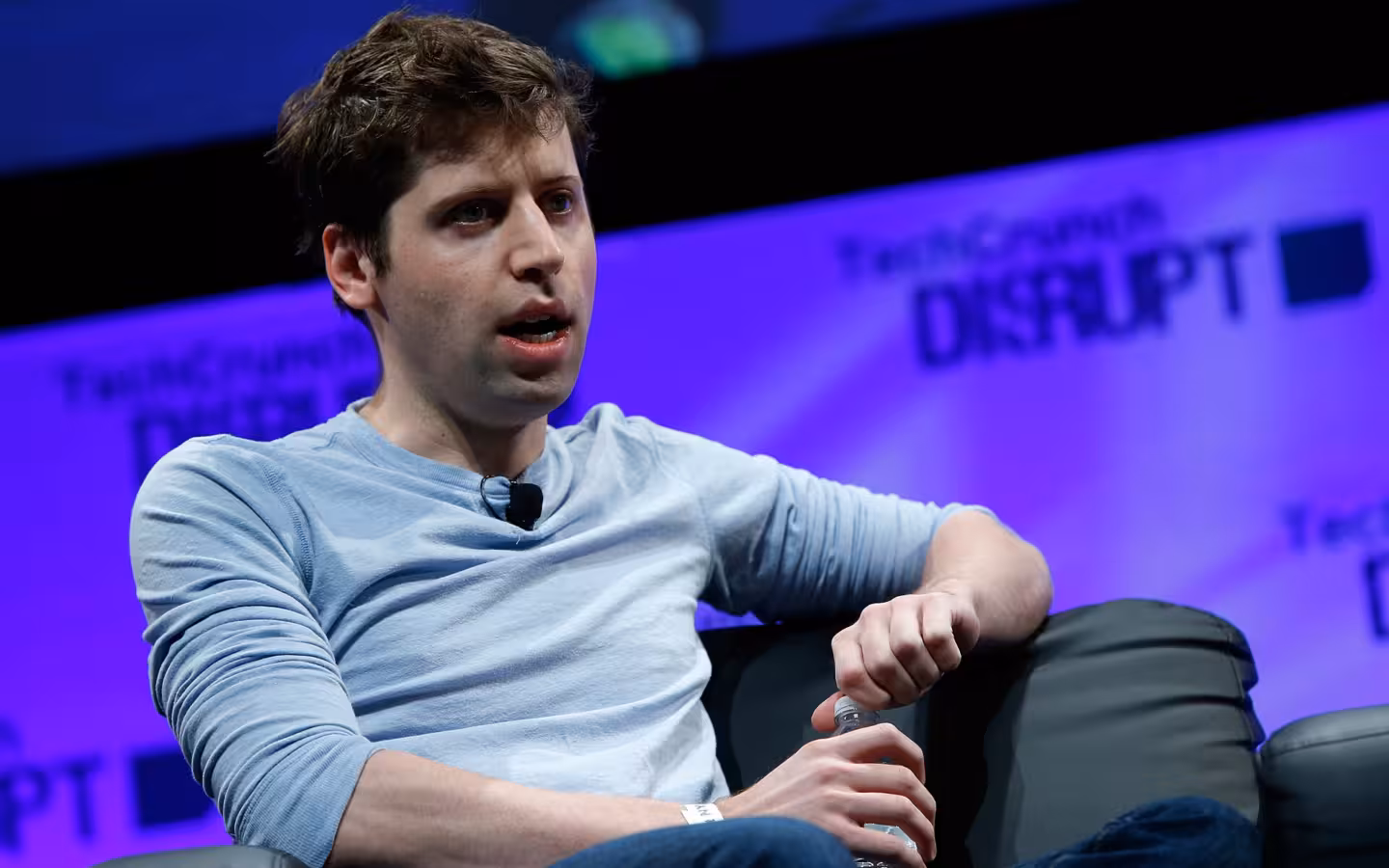 Sam Altman speaking onstage before a purple TechCrunch Disrupt backdrop