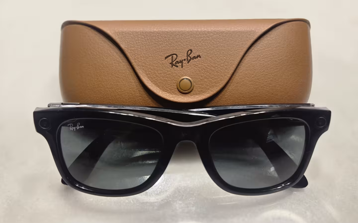 Black Ray-Ban Meta Gen 1 smart glasses in front of their brown charging case.