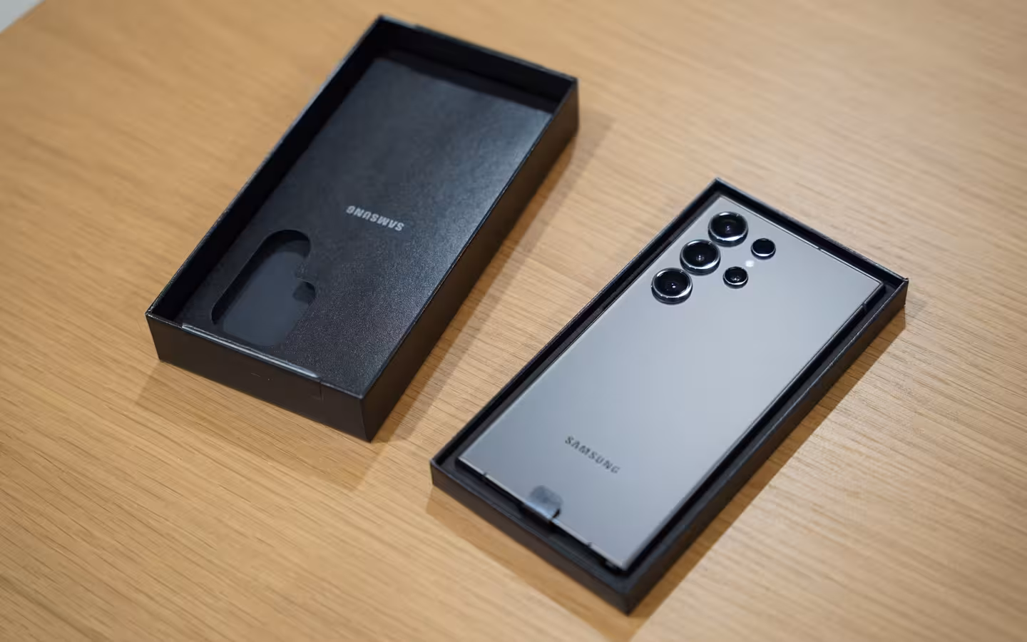 A Samsung Galaxy S24 Ultra lies beside its retail box on a wooden table.