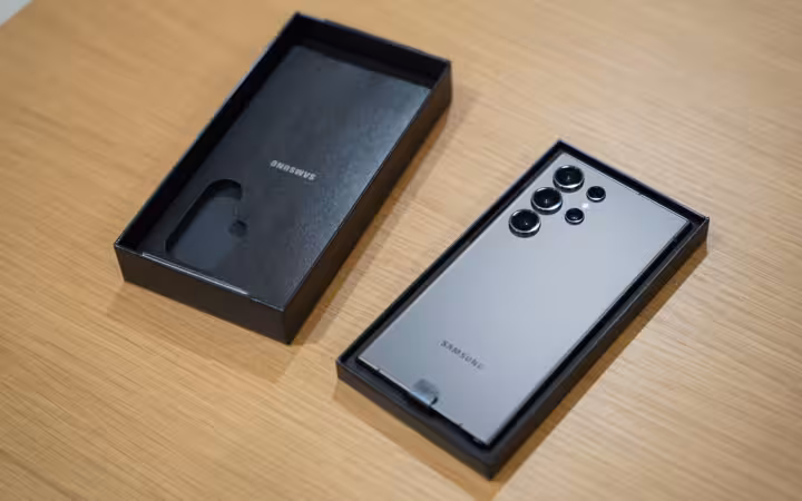 A Samsung Galaxy S24 Ultra lies beside its retail box on a wooden table.