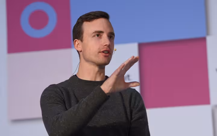 Andrew Reed speaking onstage with a headset microphone against a colorful backdrop