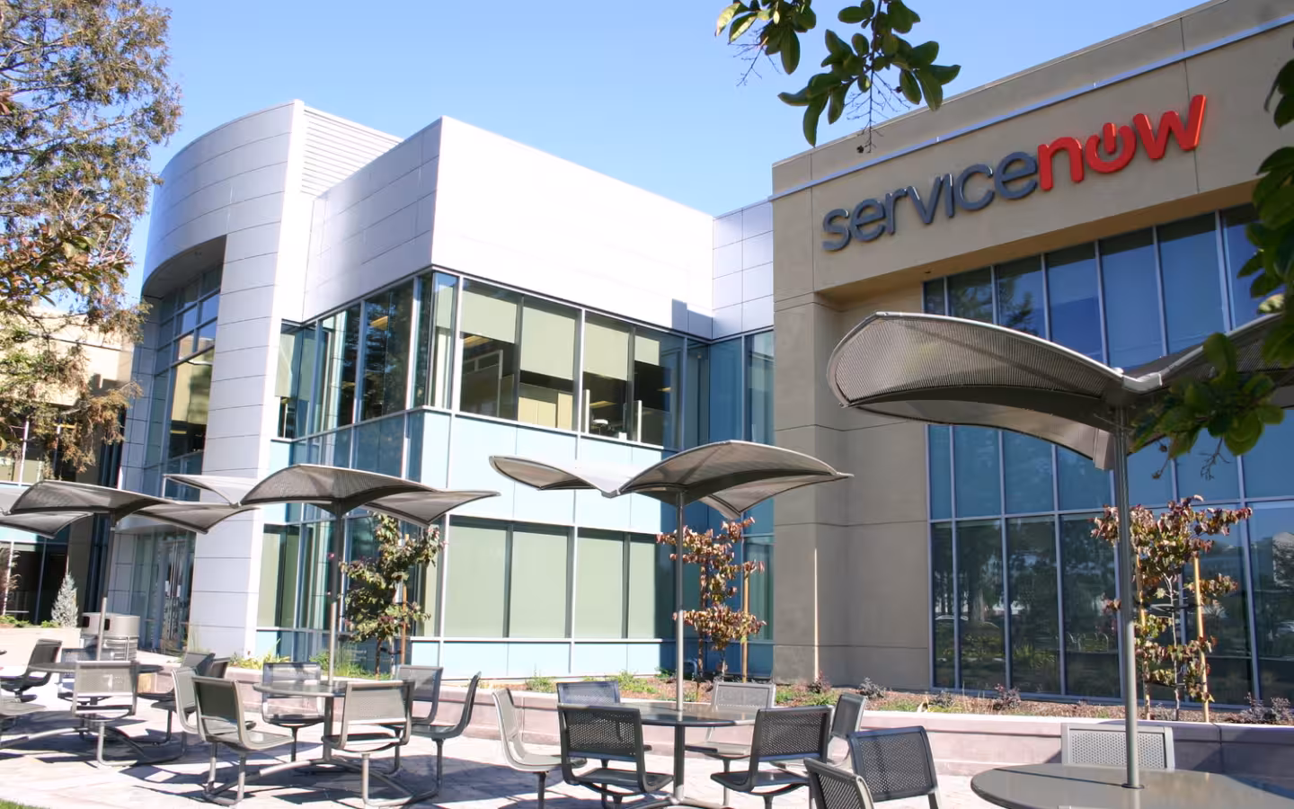ServiceNow headquarters building with a prominent logo, glass windows and patio umbrellas
