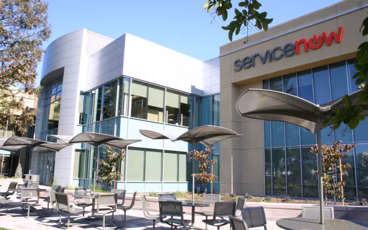 ServiceNow headquarters building with a prominent logo, glass windows and patio umbrellas
