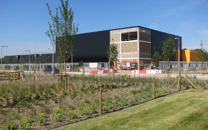 A data centre under construction in West Cambridge behind fencing and young trees