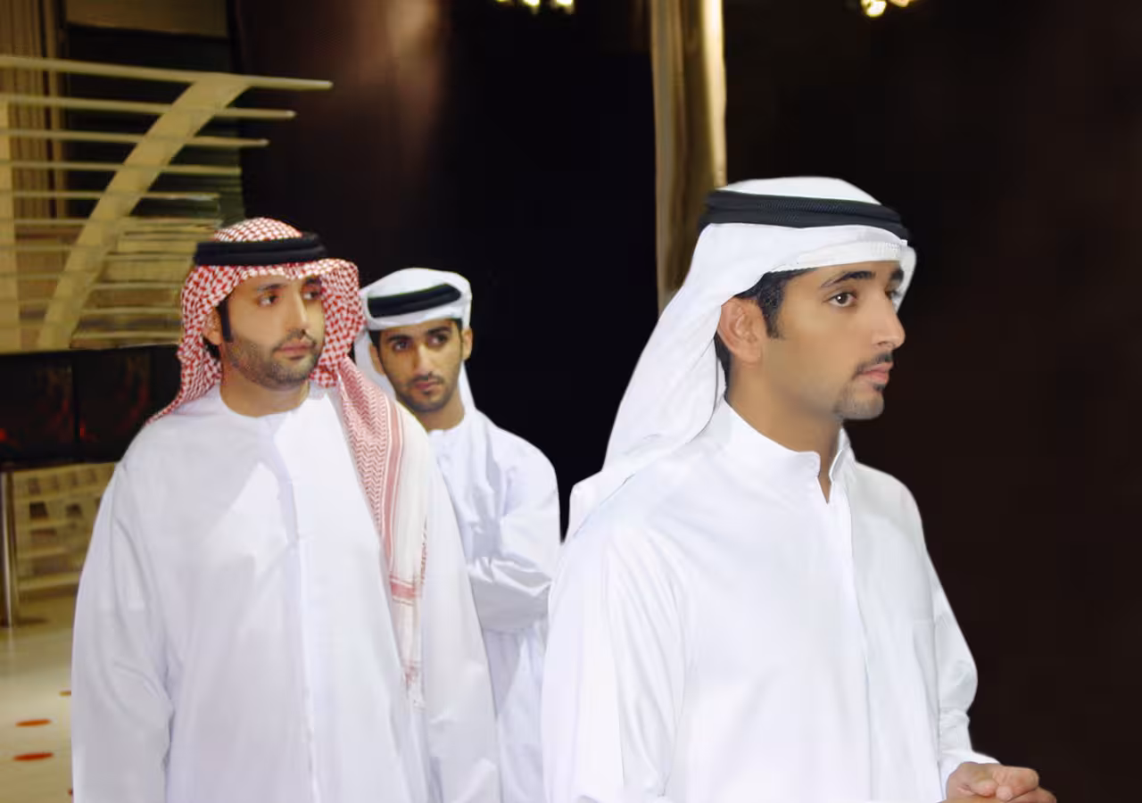 Three men in traditional attire stand indoors, including Sheikh Hamdan and Suhail Al Zarooni.