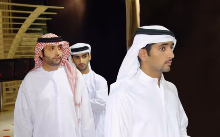 Three men in traditional attire stand indoors, including Sheikh Hamdan and Suhail Al Zarooni.