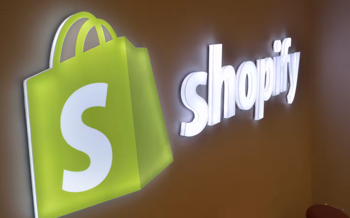 An illuminated Shopify logo and wordmark mounted on an office wall.