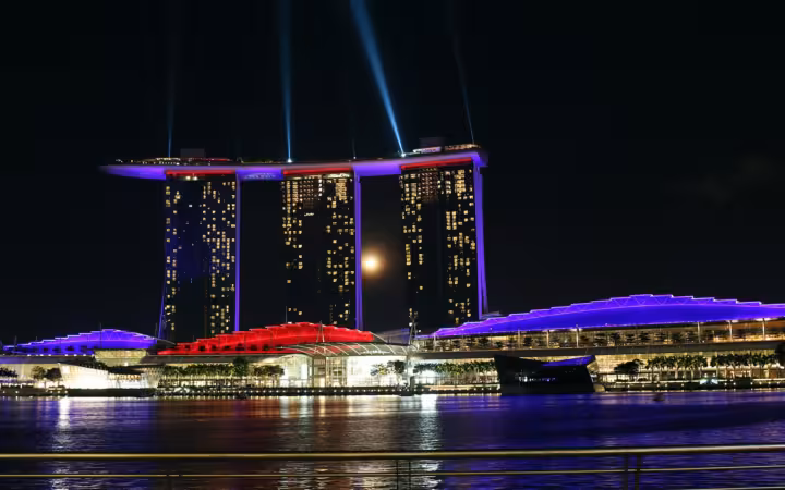Marina Bay Sands illuminated at night, with light beams above the waterfront.