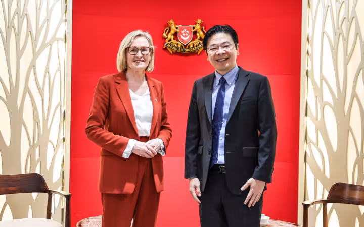 Mairead McGuinness and Lawrence Wong stand smiling beneath Singapore’s coat of arms.