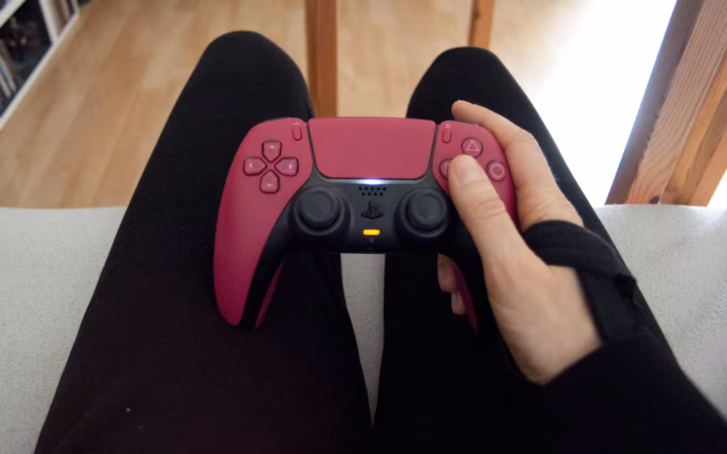 A person wearing a wrist brace holds a pink PlayStation 5 controller.