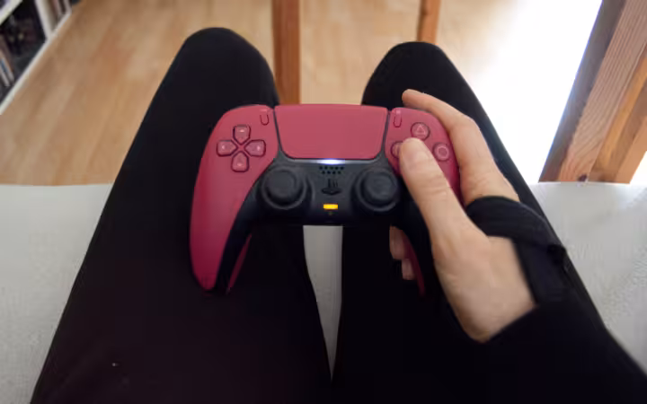 A person wearing a wrist brace holds a pink PlayStation 5 controller.
