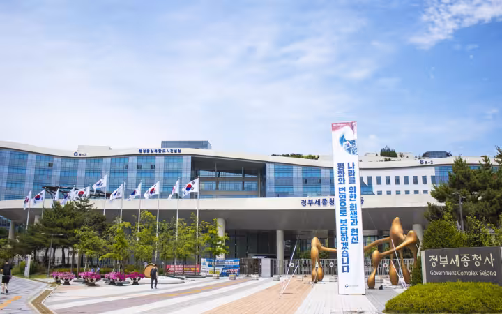 Government Complex Sejong entrance with flags, a tall banner and a wide plaza
