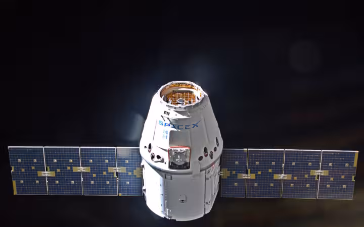 A SpaceX Dragon supply spacecraft with solar arrays against black space