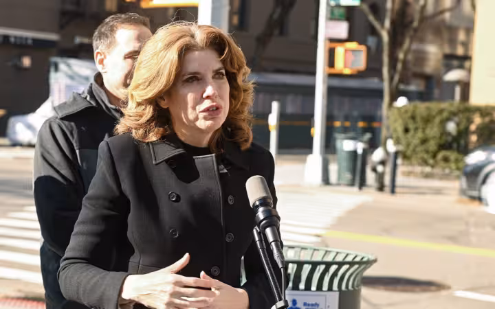 City Council Member Julie Menin speaking at a microphone on a city street.