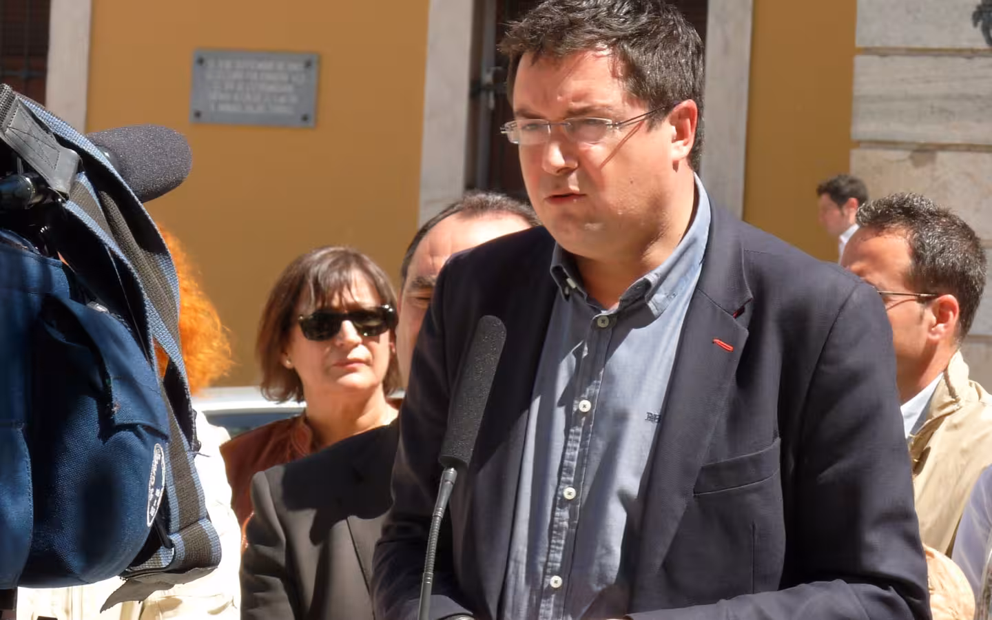 Óscar López speaks into a microphone outdoors as cameras and onlookers crowd around.