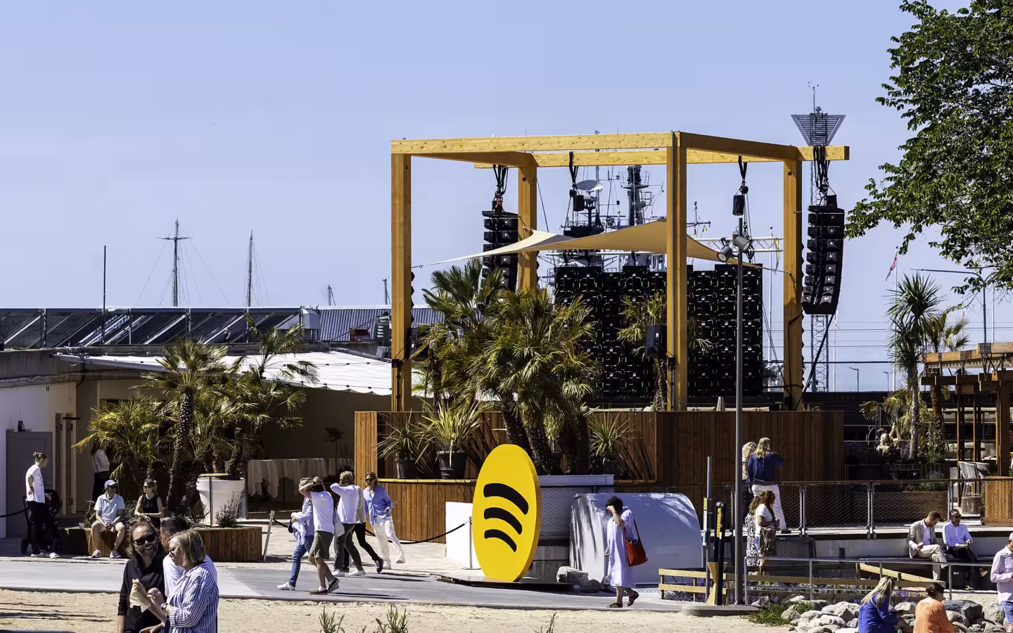 Spotify’s yellow logo stands before an outdoor stage and scattered visitors.
